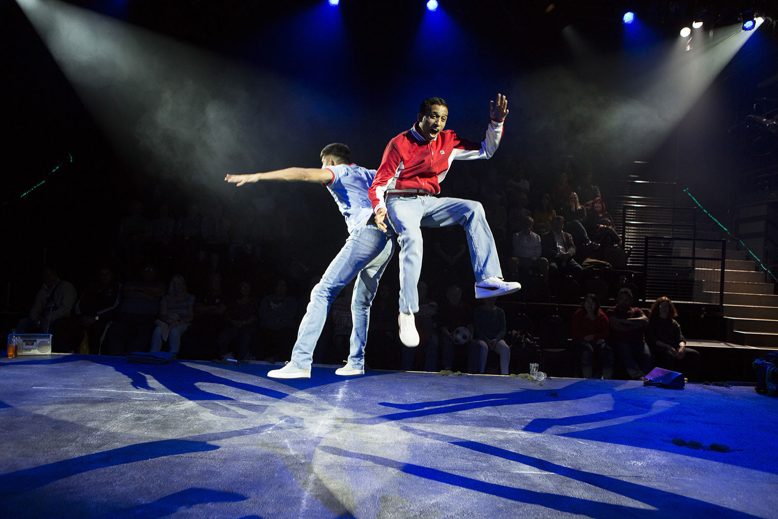 Two male actors from Memoirs of An Asian Football Casual triumphantly jumping in the air whilst facing back to back.