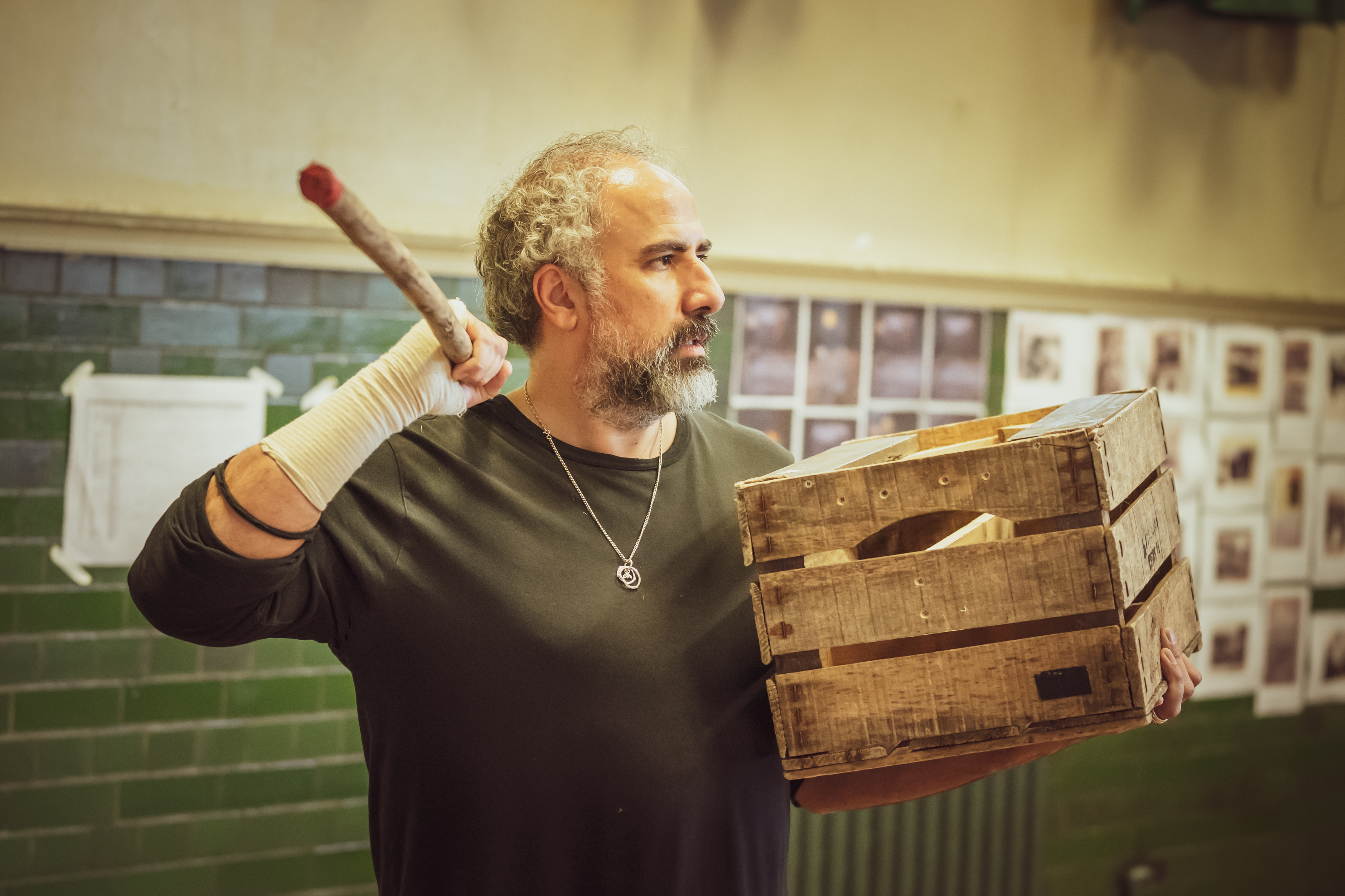 Male cast member holding a stick in one hand whilst holding a wooden box in the other