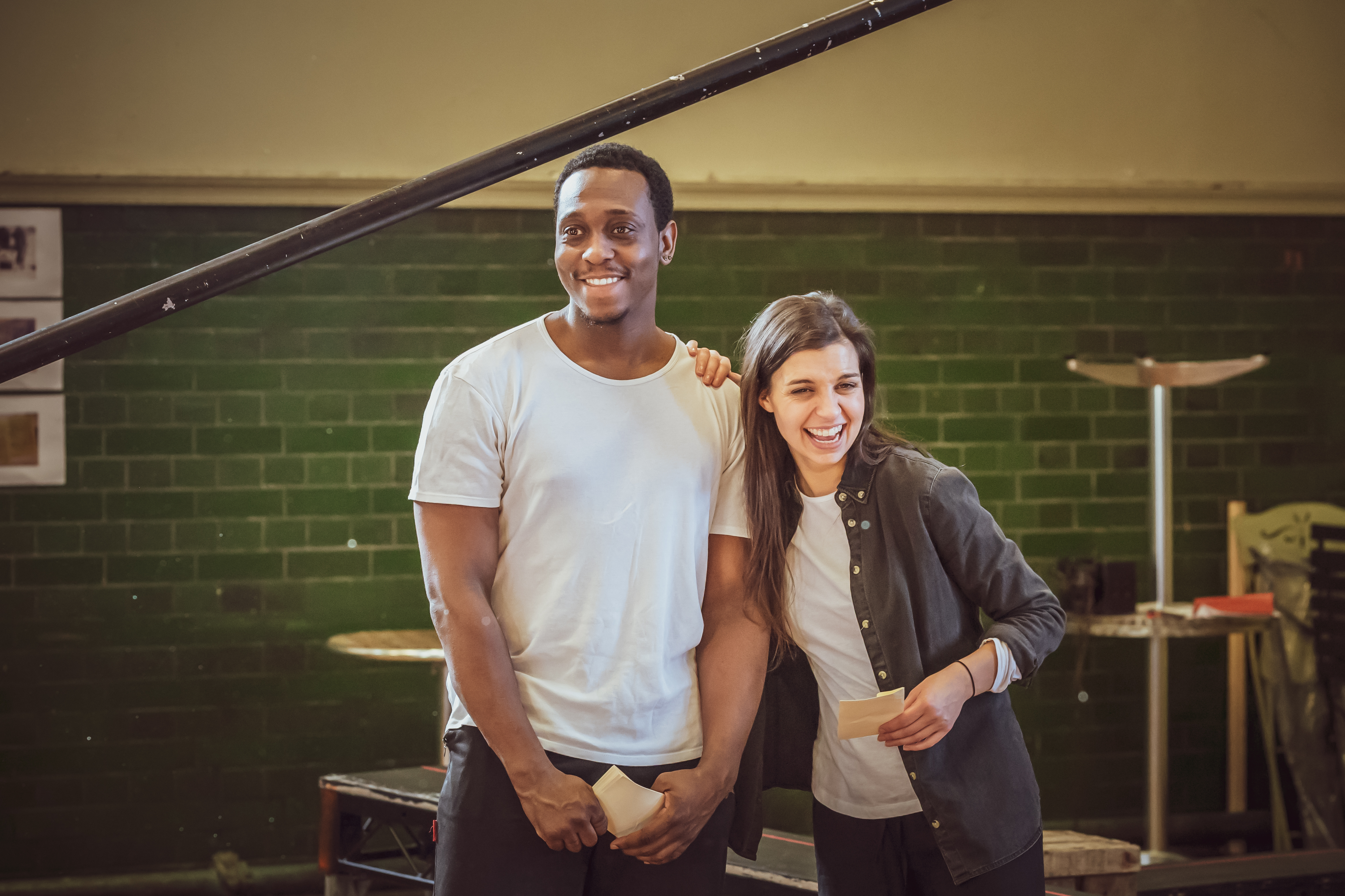 a male and female cast member standing side by side looking in opposite directions and chuckling