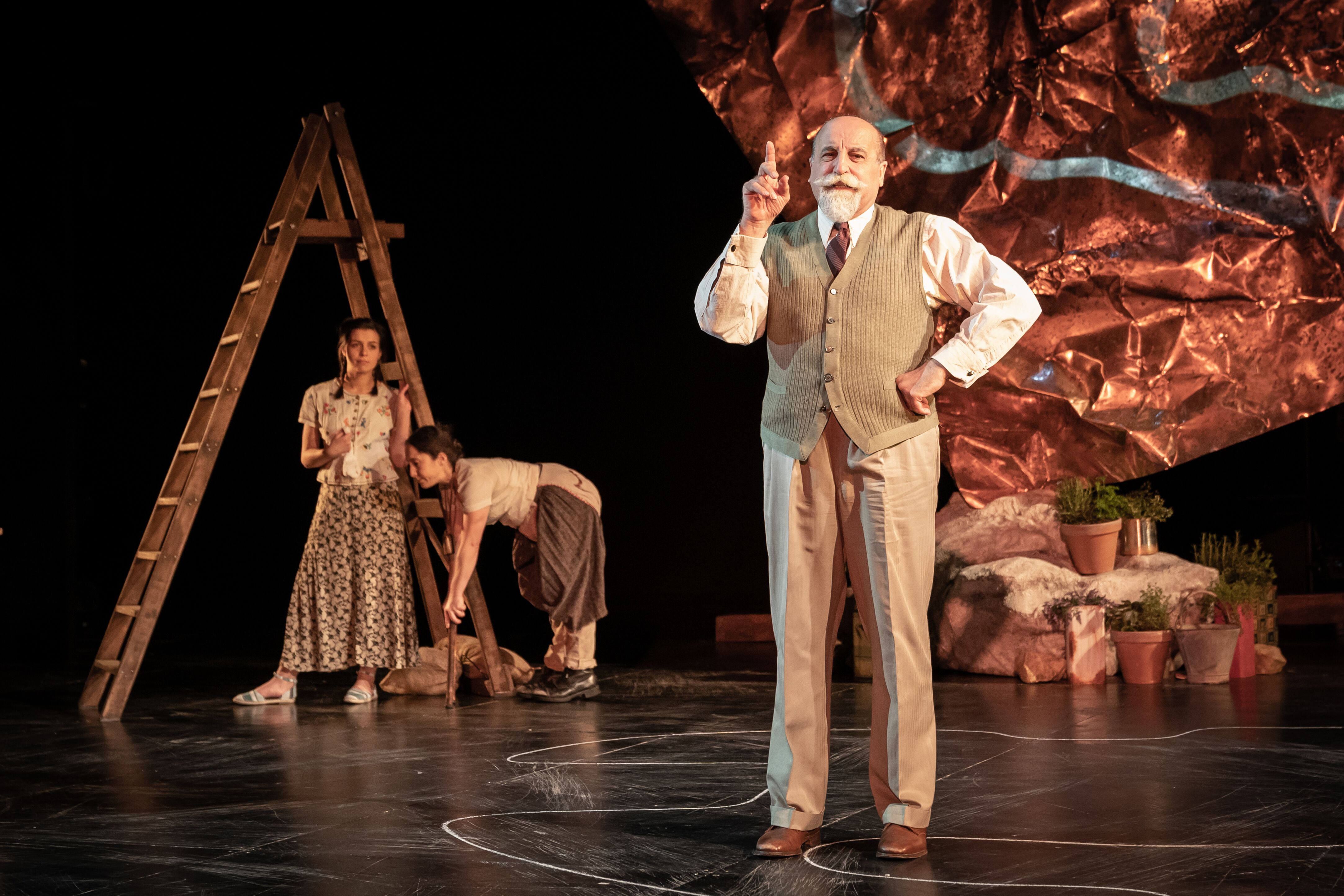 an elderly man with a white moustache dressed in a sand colored suit with one hand pointing in the air