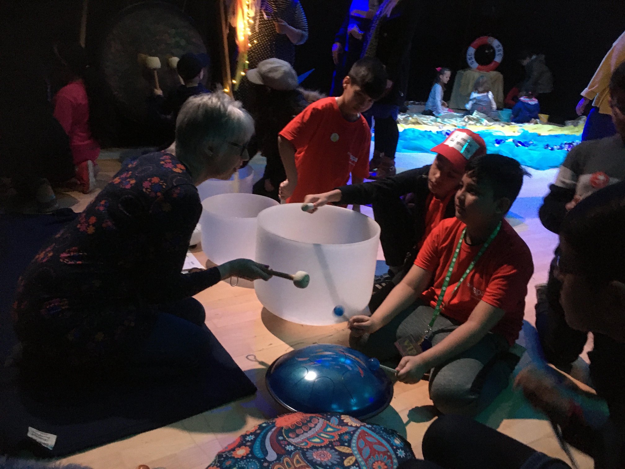 Three children being shown an unusual musical instrument by an adult.