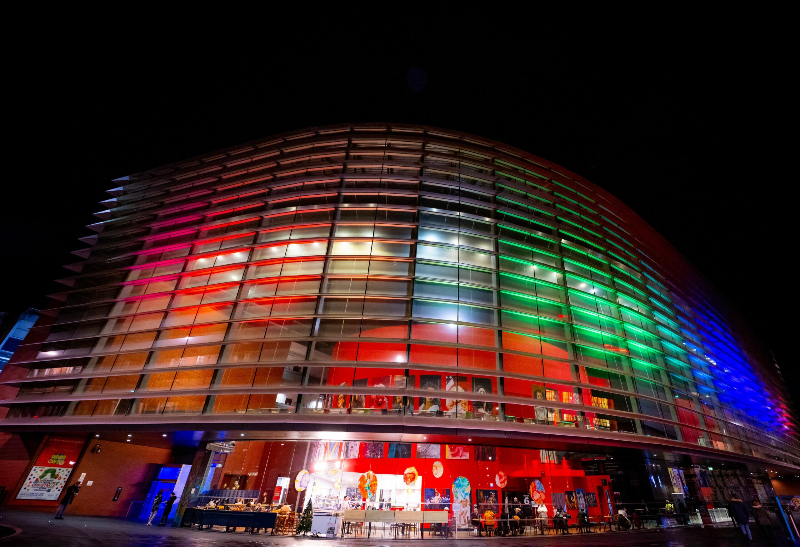 Exterior night-time image of Curve illuminated in rainbow lights.