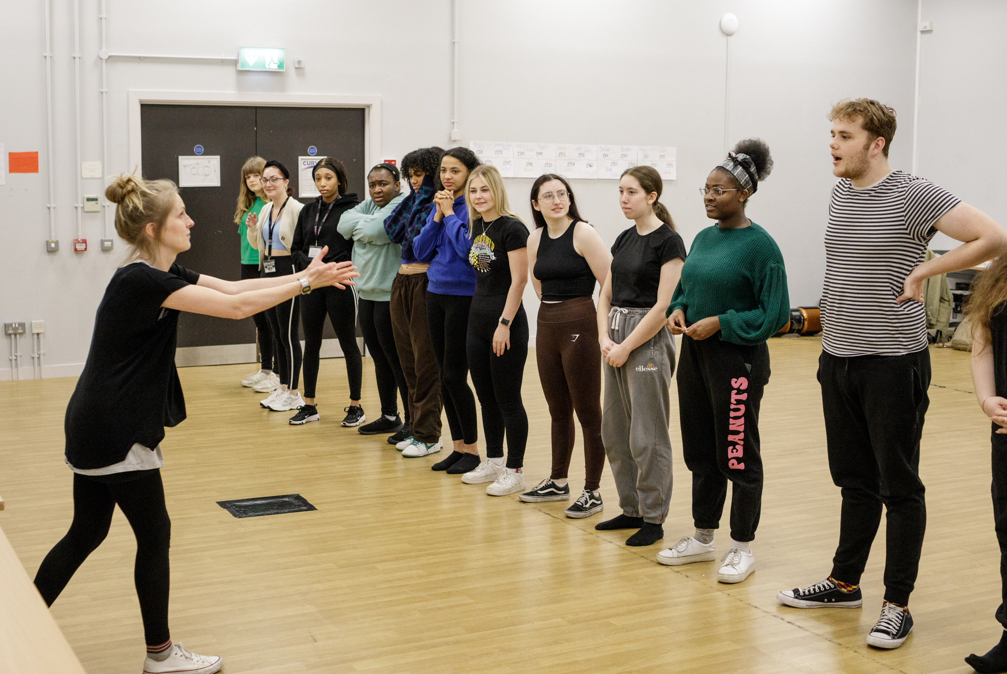 Students stand in a line as director Cara Nolan raises her arms in front of them.