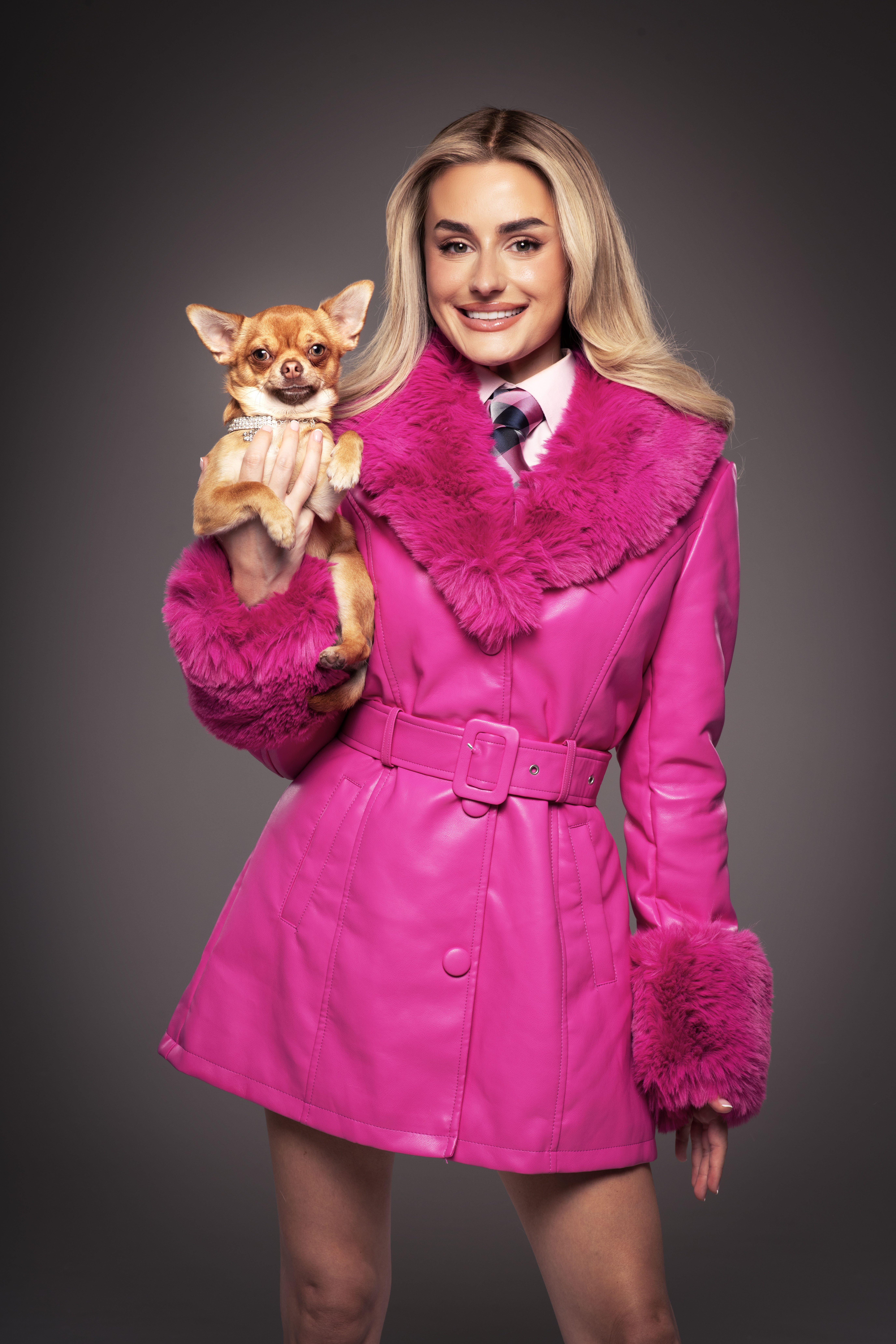 Amber Davies as Elle Woods, wearing a bright pink coat and holding a chihuahua.